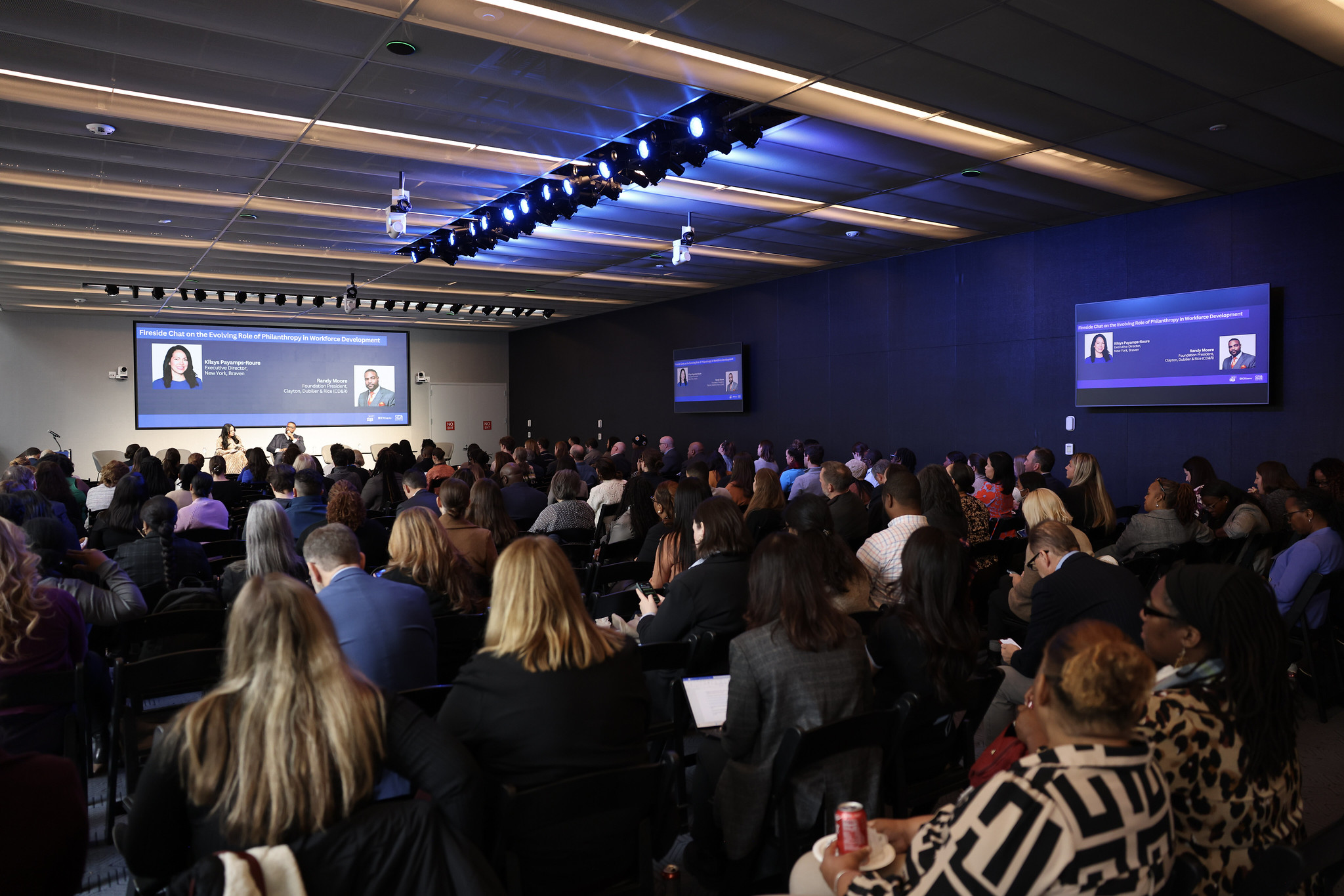 Civic Halls main auditorium space with blue lighting filled with attendees in theater style seating facing the stage at the 2024 NYCETC Conference