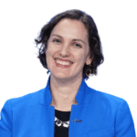 Caitlyn Brazill with short brown hair smiles with reddish color lipstick wearing a cobalt blue blazer and black shirt with a small Per Scholas pin on her lapel.
