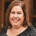 Marci Hunn with shoulder-length brown hair, wearing a sparkly black top, photographed in warm outdoor light.