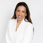 Therese Daly smiles with long brown hair in a white blazer.