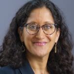 Angie Kamath with dark rimmed glasses and medium length curly hair.