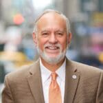CUNY Chancellor Félix V. Matos Rodríguez with grey hair and beard in a beige suit with a peach color tie.
