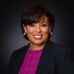 Grace Bonilla with short brown hair, a pink checkered shirt, and navy-colored blazer.