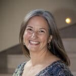 Jennifer Mitchell with long light hair smiles in a beaded blue and white top.