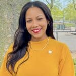 Amanda Septimo in a bright yellow long sleeve shirt, with long brown hair and red lipstick.