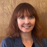 Stacey Nodelman with a navy blue blazer and red long hair.